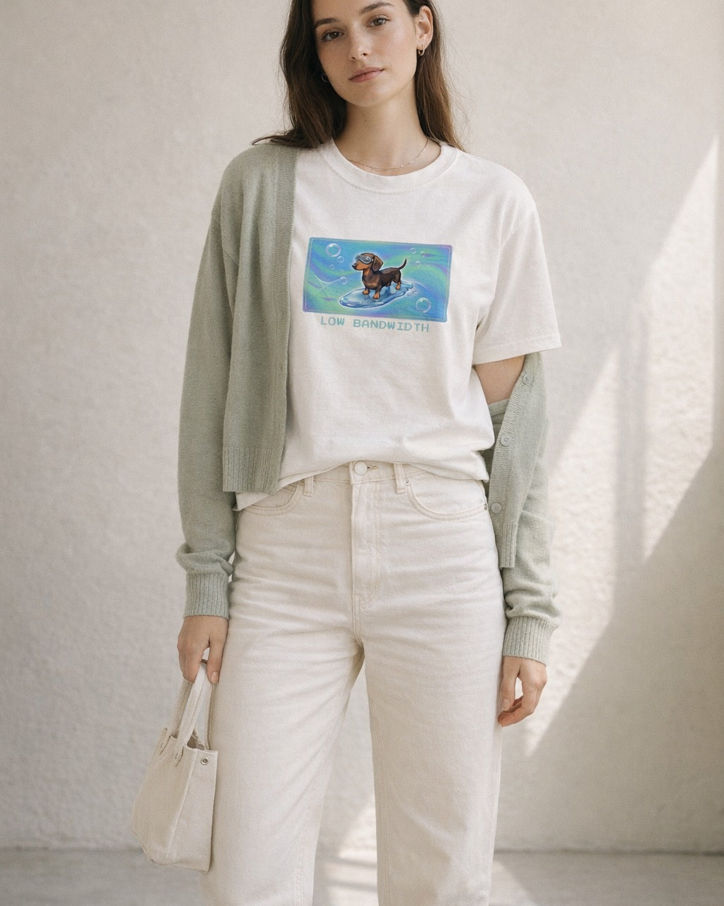 O's Tees Low Bandwidth Dachshund Frutiger Aero Dogs graphic tee lifestyle image — White shirt, female shot 02, sage cardigan cream denim